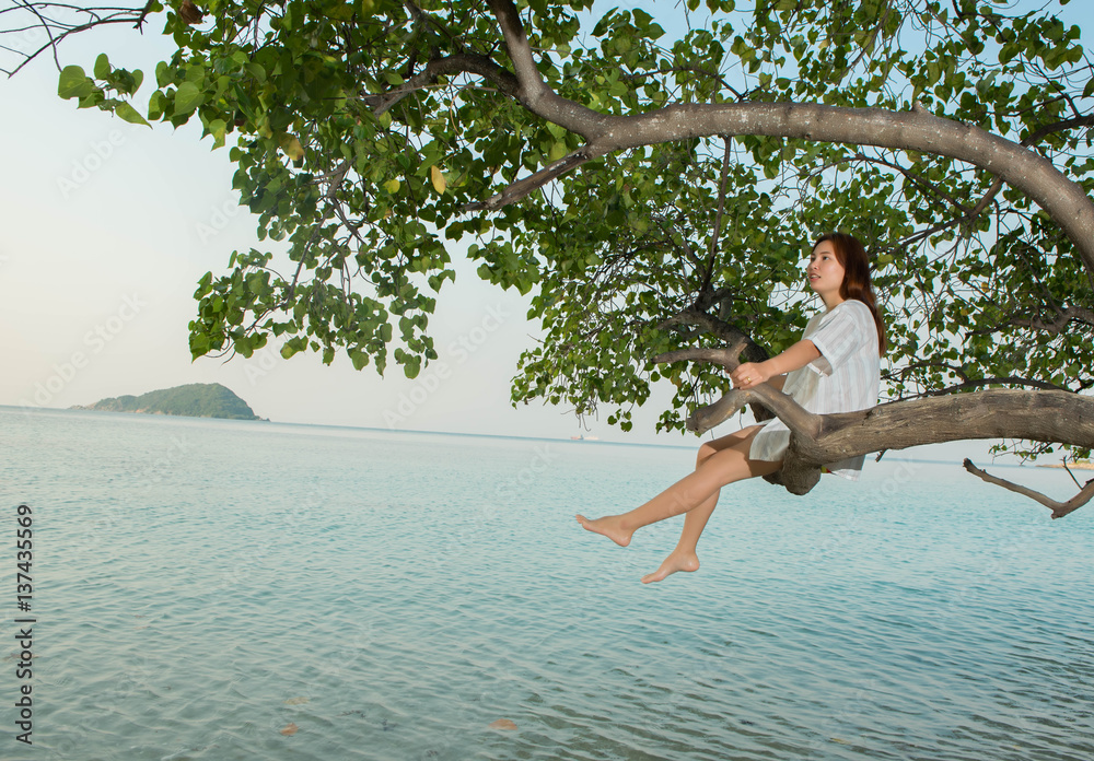 Obraz premium young woman sitting back on tree with the sea