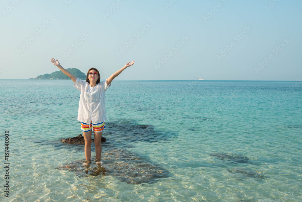 Happy woman standing arms outstretched on the beach at Sea