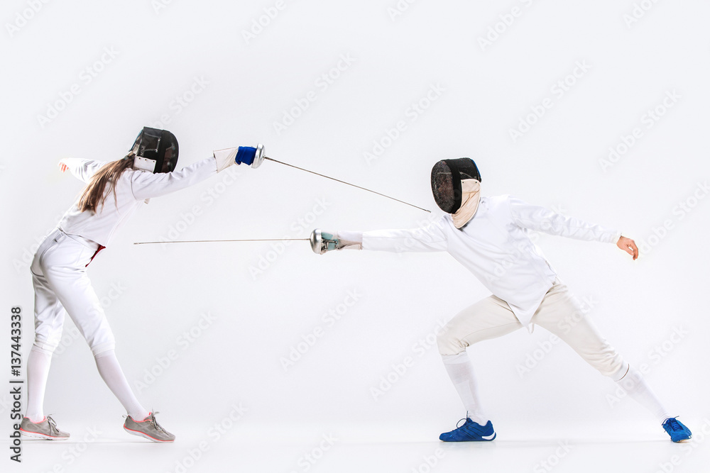 The woman and man wearing fencing suit practicing with sword against gray The woman and man wearing fencing suit practicing with sword against gray
