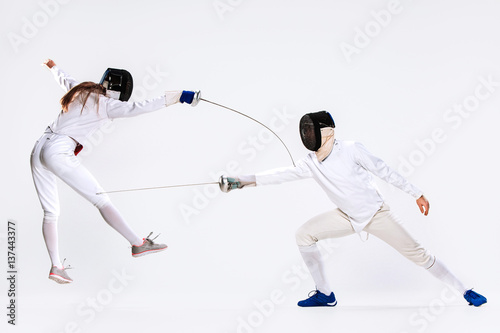 The woman and man wearing fencing suit practicing with sword against gray