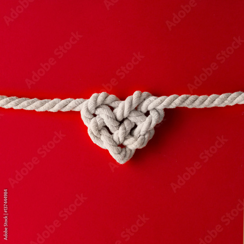 White rope in heart shape knot on red background. Love concept. Flat lay.