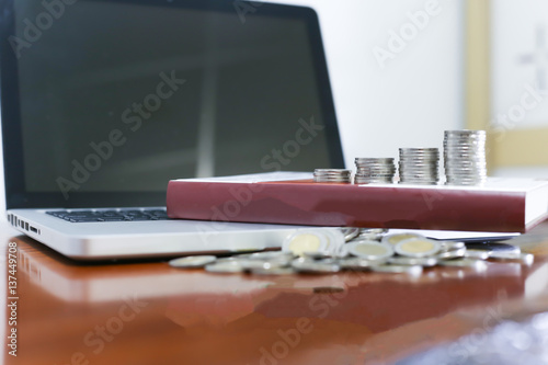 Business concept. Closeup stack of coins, laptop  and old book on wooden table.