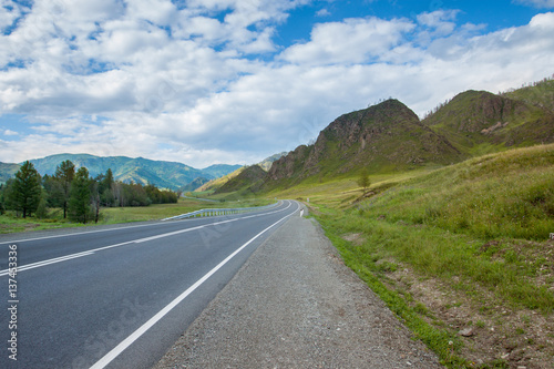 Beautiful road in the mountains. Mountain landscape on the Chuyskiy Tract in the Altai mountains. On the road a sharp turn, around the beautiful mountains and cloudy sky. 