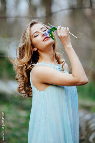 attractive model in blue dress smell snowdrop flowers in the spring forest