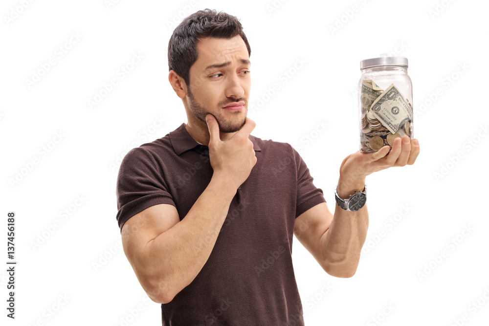 Pensive man looking at a jar filled with money Pensive man looking at a jar filled with money