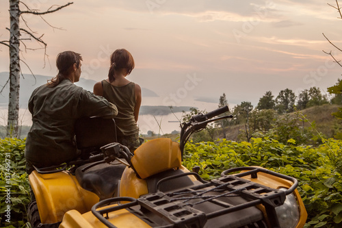 Beautiful couple is watching the sunset from the mountain sitting on a quadbike.