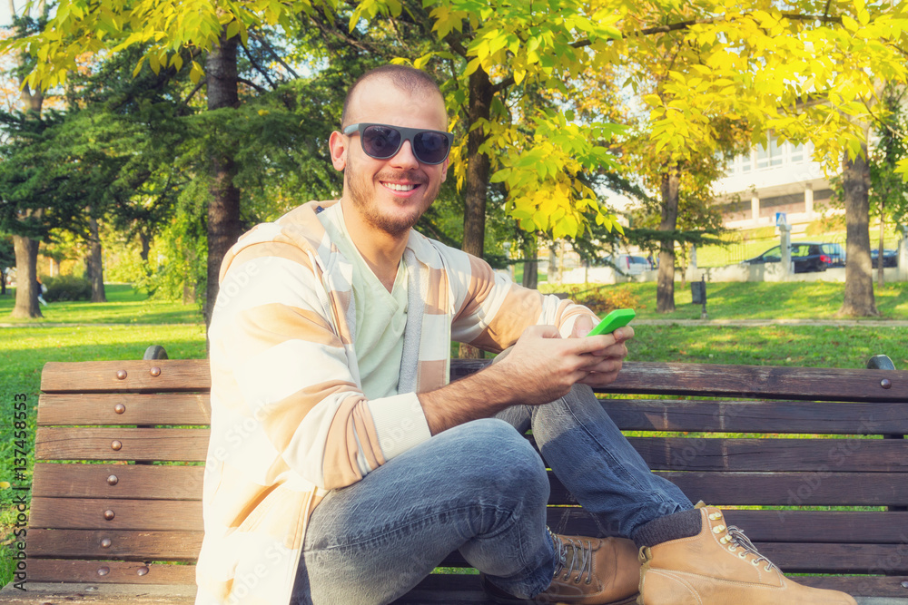 Obraz premium Man using cellphone on a bench in the park.