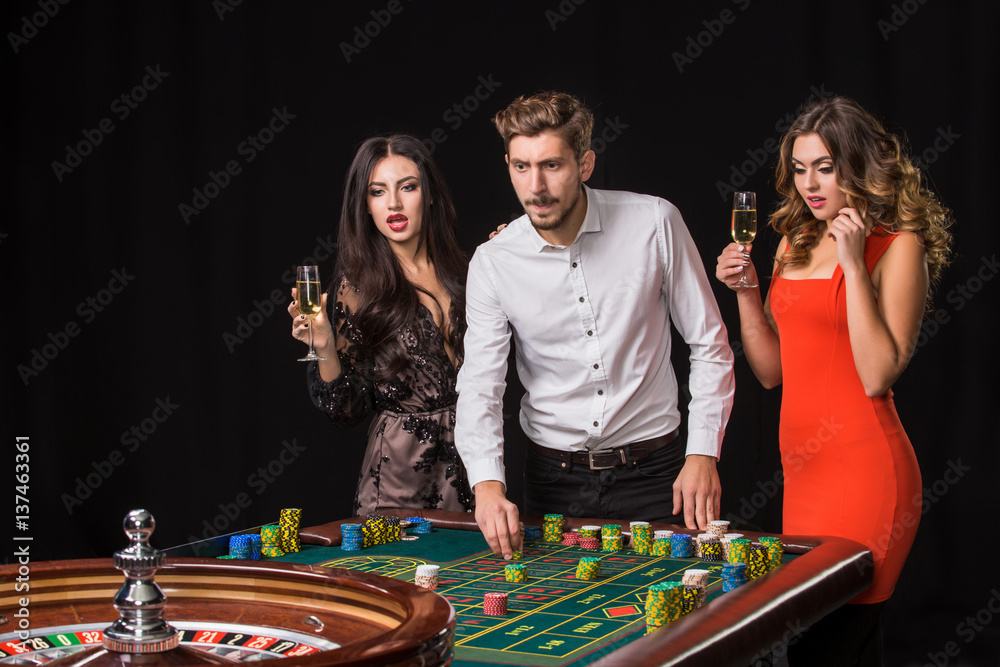 Two young women and man behind roulette table on black background Two young women and man behind roulette table on black background