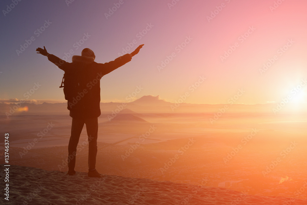 male traveler is standing on top of a mountain with a backpack and put his hands up