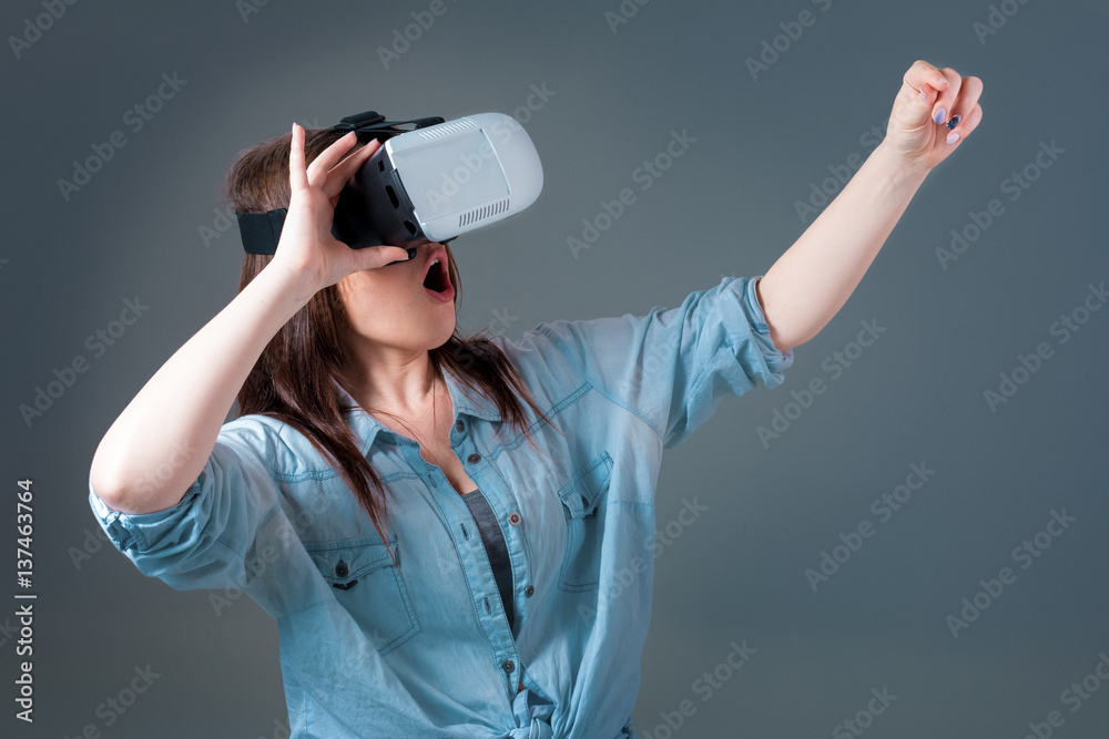 Emotional young woman using a VR headset and experiencing virtual reality on grey background Emotional young woman using a VR headset and experiencing virtual reality on grey background