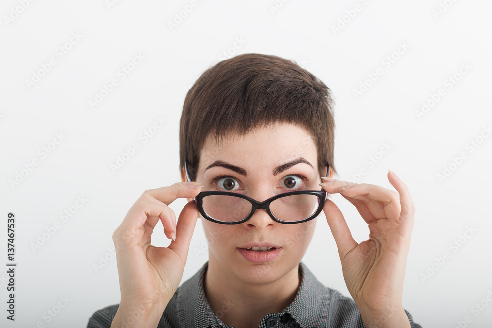 Close up of strict surprised young funny female teacher or student in glasses isolated on white background, looking over her glasses Close up of strict surprised young funny female teacher or student in glasses isolated on white background, looking over her glasses