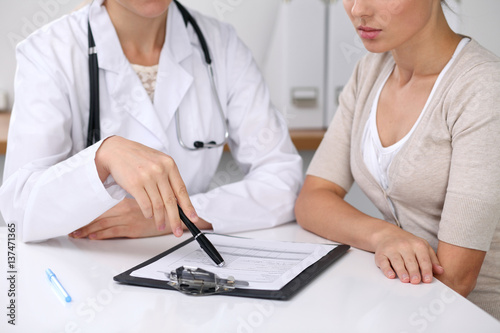 Close up of doctor and patient sitting at the desk while physician pointing into medical form hystory. Medicine and health care concept