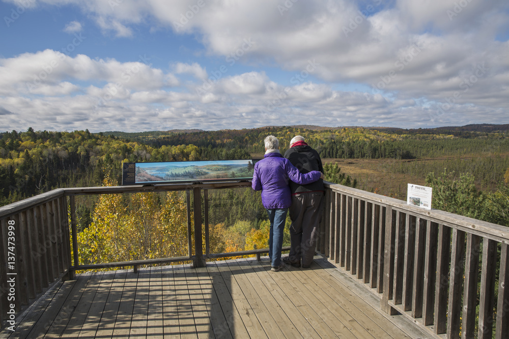 Mature couple overlooking Sunday Creek from the Algonquin Park visitor centre observation deck on a sunny afternoon in autumn; Ontario, Canada Mature couple overlooking Sunday Creek from the Algonquin Park visitor centre observation deck on a sunny afternoon in autumn; Ontario, Canada