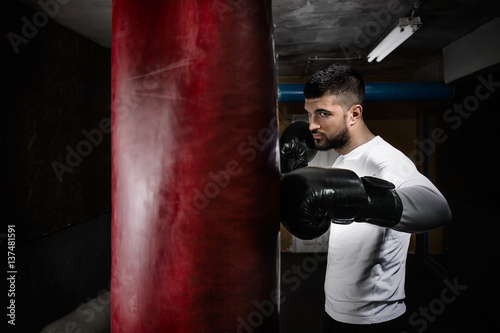 Portrait of young man exercising at the gym. He is practicing with boxing gloves and punching bag © bokan