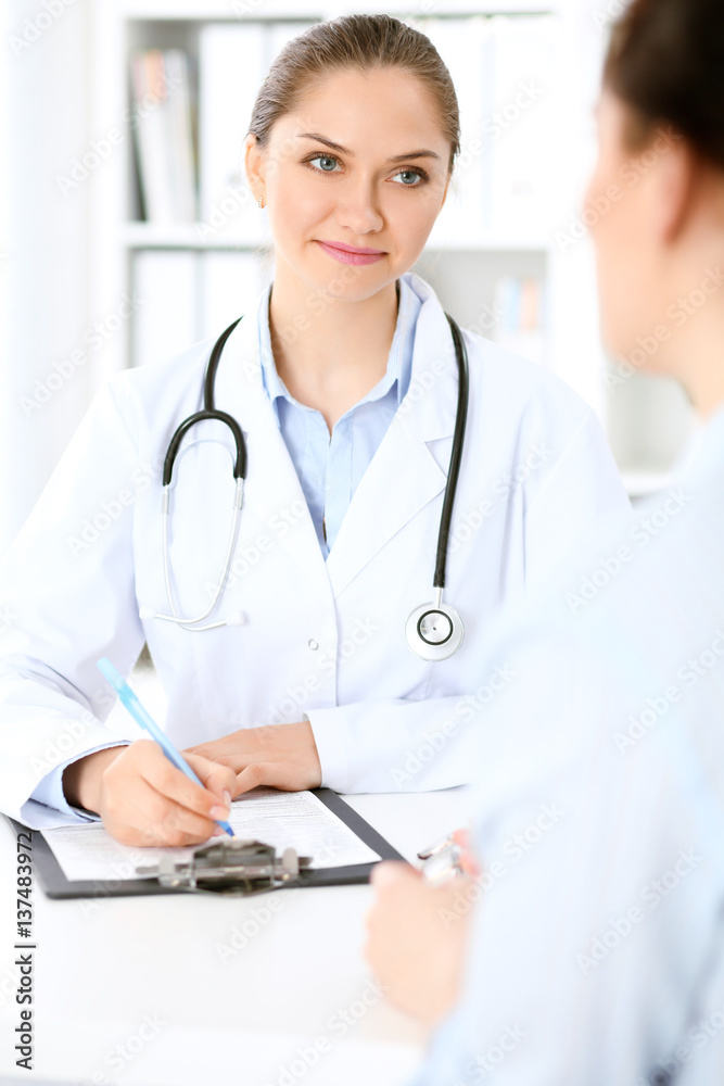 Friendly smiling doctor and patient sitting at the table. Very good news and high level medical service concept. Friendly smiling doctor and patient sitting at the table. Very good news and high level medical service concept.