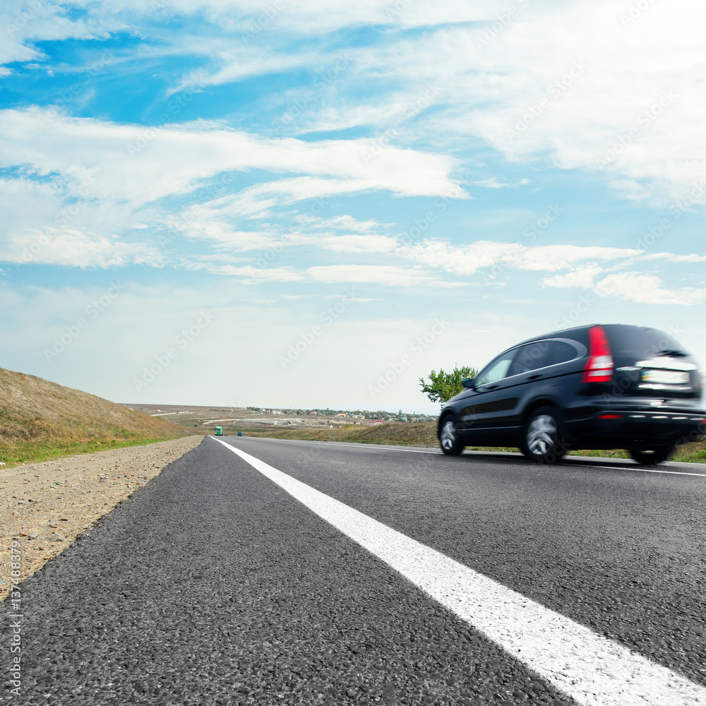 black car in motion on asphalt road and blue sky with clouds