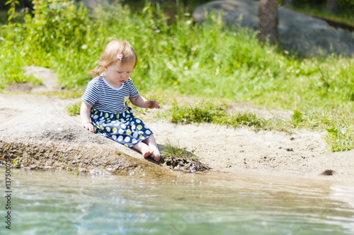 Fototapeta Naklejka Na Ścianę i Meble -  Little girl sitting on a river bank in the summer