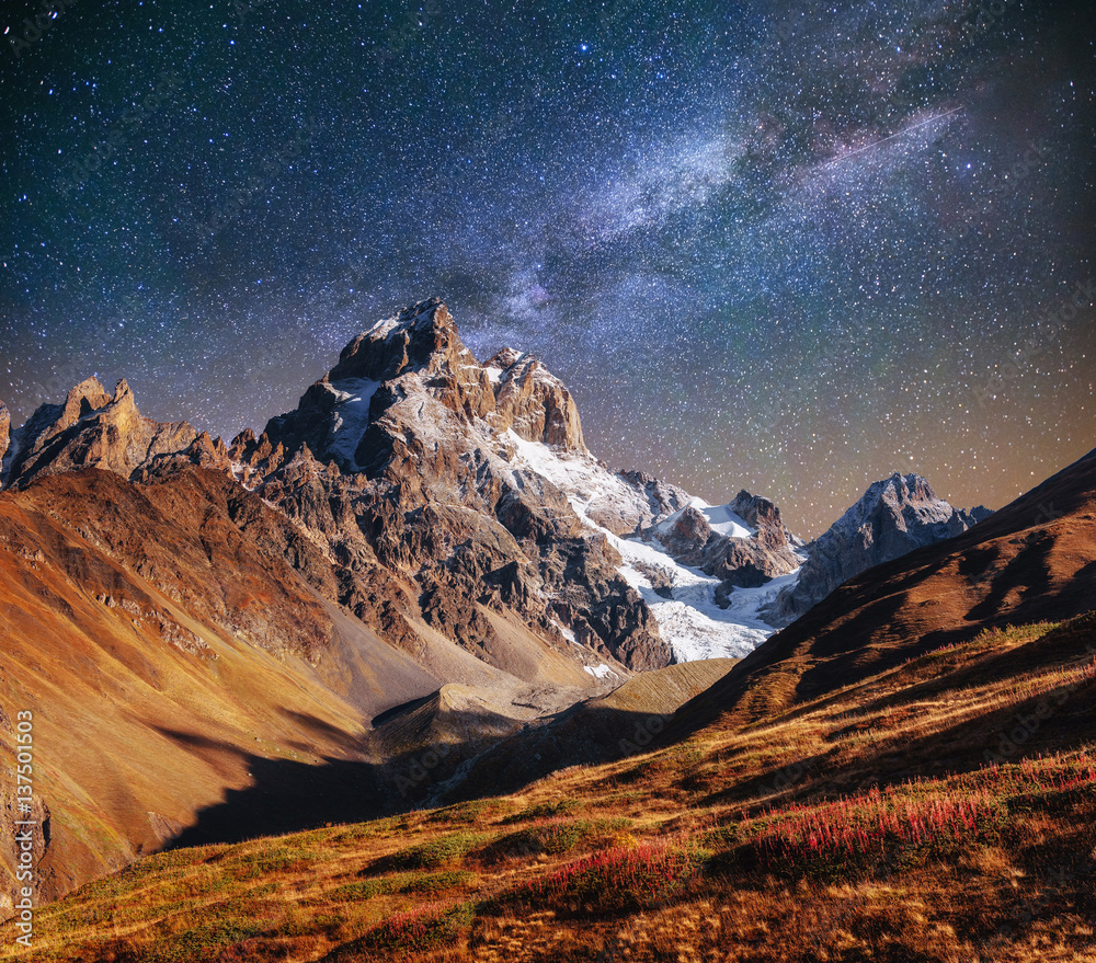 Fantastic starry sky. Autumn landscape and snow-capped peaks. Ma