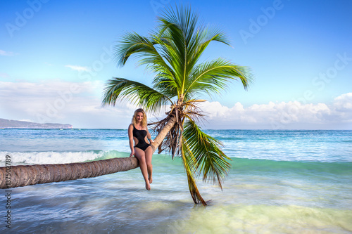 young sexy girl sitting on palm tree over blue sea photo