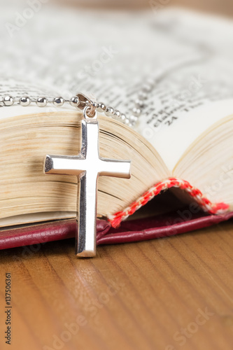 Necklace with silver cross on wooden table and opened bible book