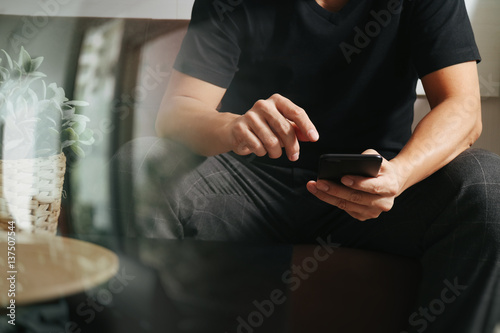 designer man hand using smart phon for mobile payments online shopping,omni channel,sitting on sofa in living room,vase rattan with plant and wooden tray on table,filter