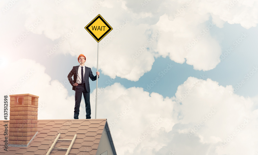 Young businessman on house brick roof holding yellow signboard. Young businessman on house brick roof holding yellow signboard.