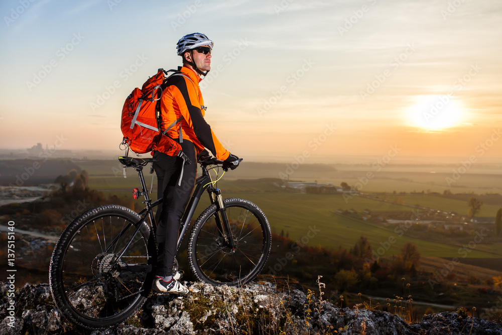 View of cyclist standing with mountain bike on hill trail at sunset