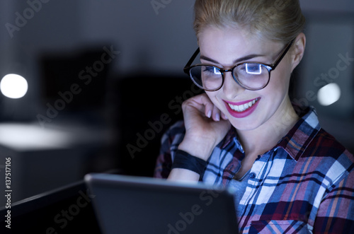 Amused IT girl using gadget in the dark lighted room