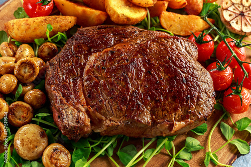 Photography Cooked Beef Ribeye Steak with Potato, Mushrooms, tomatoes on wooden board