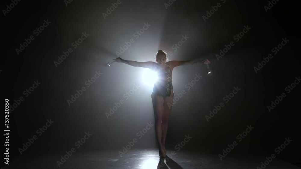Girl gymnast with mace in hand revolve around him. Black background. Light rear. Silhouette Girl gymnast with mace in hand revolve around him. Black background. Light rear. Silhouette