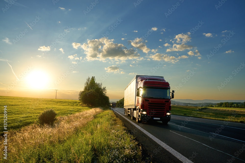 Arriving red truck on the road in a rural landscape at sunset