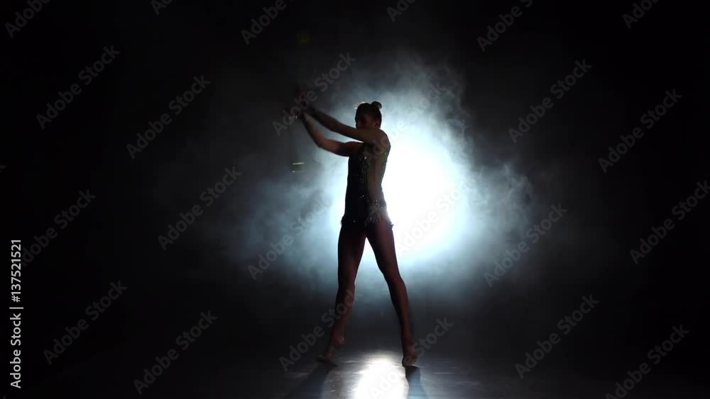 Girl gymnast with mace in hand revolve around him. Black background. Light rear. Silhouette. Slow motion Girl gymnast with mace in hand revolve around him. Black background. Light rear. Silhouette. Slow motion