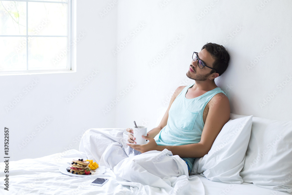 Young man having pancakes in bed and coffee