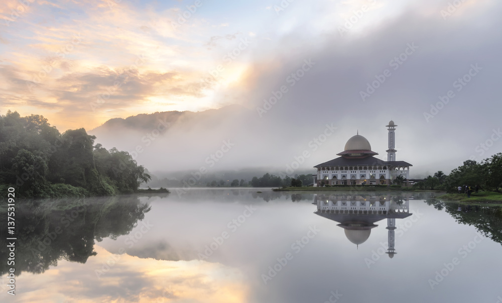 Fototapeta premium View and reflection of Darul Quran Mosque with fogs and stunning clouds during sunrise.