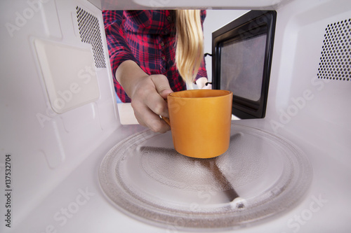 Woman opens the microwave with mug in hand