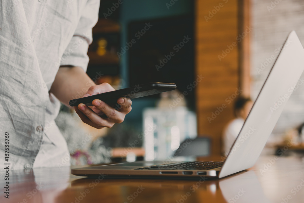 Close up of people hand using smartphone and laptop on wooden table in technology and business concept Close up of people hand using smartphone and laptop on wooden table in technology and business concept