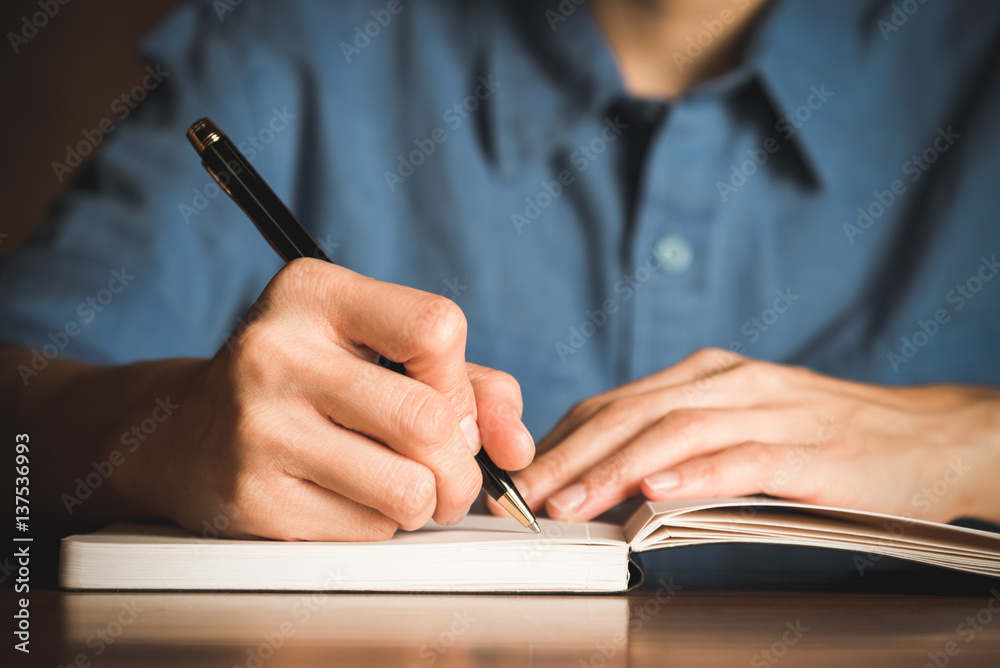 Close up of people hand writing on notebook on wooden table Close up of people hand writing on notebook on wooden table