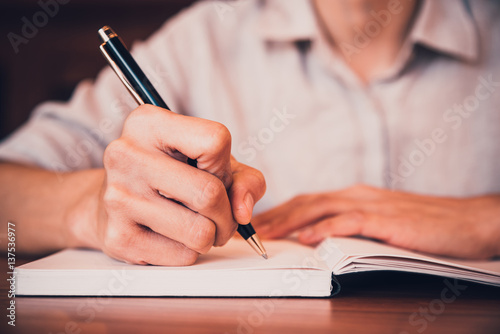 Close up of people hand writing on notebook on wooden table