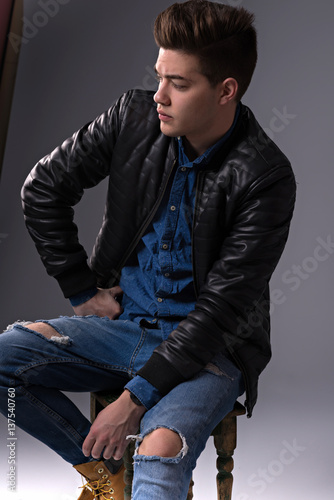 Casual young man in black jacket, jeans and boots on black background. Studio shoot.