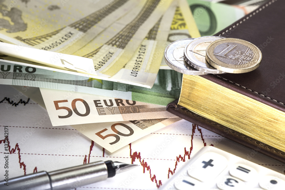 Concept of stock market exchange trading, Chart of prices with red line. Euro fifty and hundred bills lying on the graph, Notepad,fountain pen and calculator on the diagram. Euro coins on the notepad. Concept of stock market exchange trading, Chart of prices with red line. Euro fifty and hundred bills lying on the graph, Notepad,fountain pen and calculator on the diagram. Euro coins on the notepad.