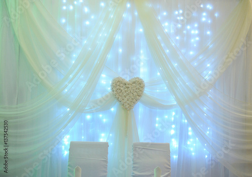 White table decor for the newlyweds in the restaurant. Backlight. Heart drapery photo