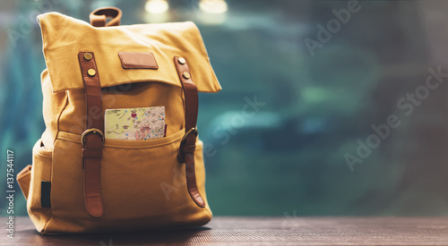 Hipster yellow backpack and map closeup. View from front tourist traveler bag on background blue sea aquarium. Person hiker visiting oceanarium museum in Barcelona on backdrop, blank blurred mockup photo
