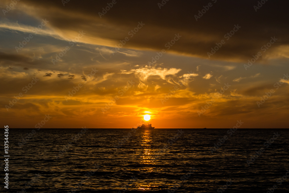 Fototapeta premium A silhouette of a ship on the horizon, a setting sun and colored orange and yellow clouds at the beach of Black sea, Sochi, Russia.