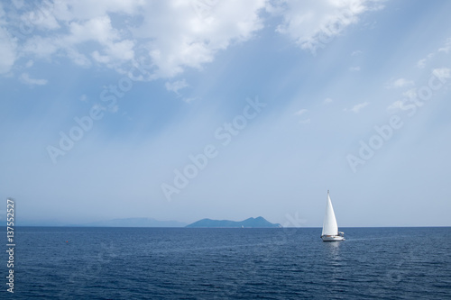Big white yacht sailing on a clam blue sea with mountains in the background and sun rays coming from the sky. Vacation on a boat. © Martin