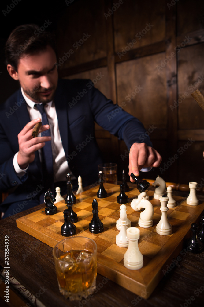 Focused man sipping alcoholic beverage while thinking about next chess move.  Stock Photo by DC_Studio