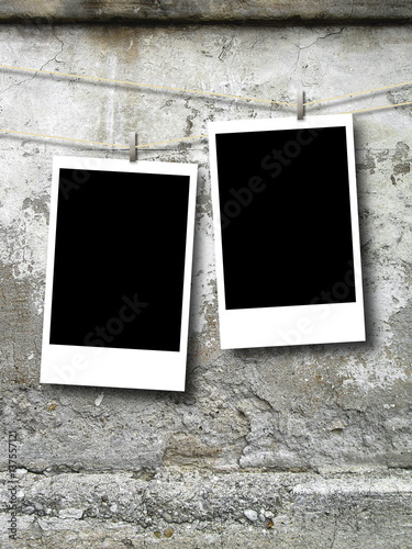 Two blank black rectangular photo frames hanged by pegs against wall