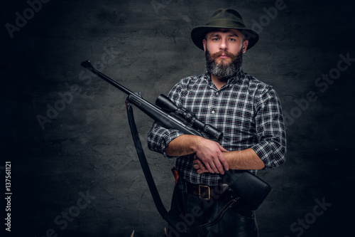 Bearded hunter holds a rifle. © Fxquadro