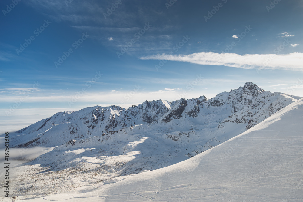 Wide shot aerial view of snow capped cold rock mountains with sunny blue skies