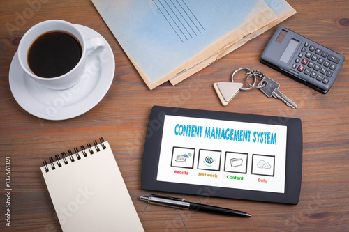 Content Management System  business concept. Text on tablet device on a wooden table.