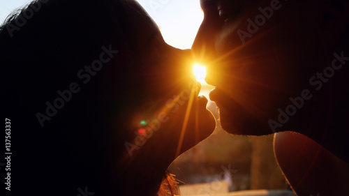 Romantic young couple silhouette is kissing on a sunset with sun shining bright behind them on a horizon. First kiss of young love.